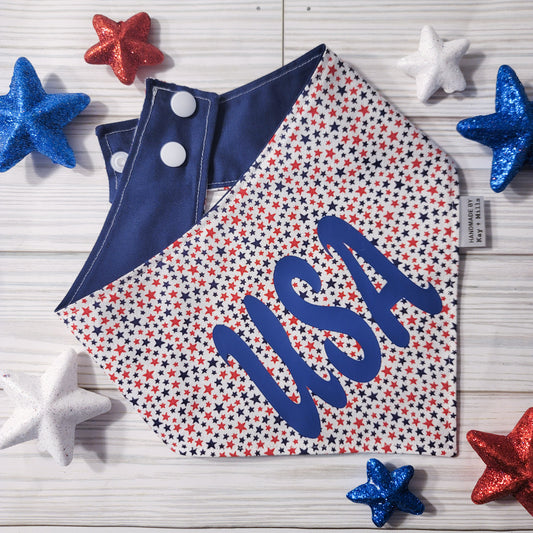Dog bandana or cat bandana with small red and navy blue stars on a white background and the letters USA in navy blue vinyl. The back of the pet bandana is navy blue and includes two sets of white plastic snaps for an adjustable fit.